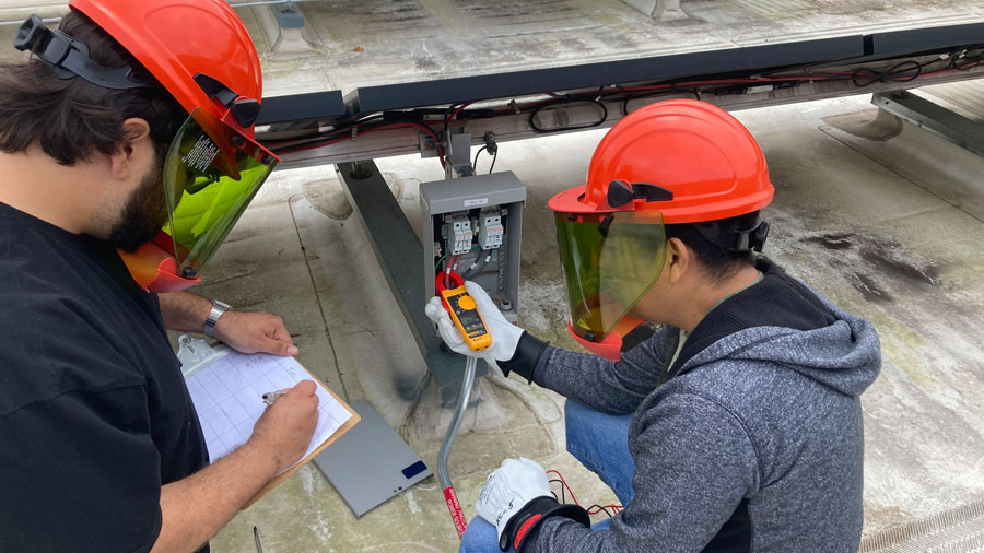 Two students working on an electrical box in the back of a solar panel array