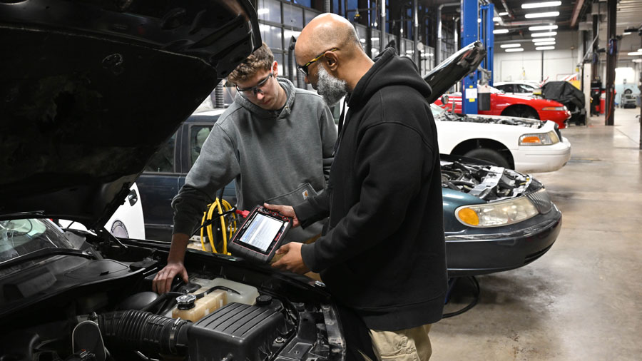 Two students using a diagnostic tool on a car they're working on