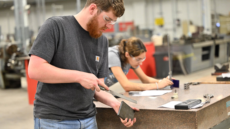 Student using a file on a piece of metal with another student in the background