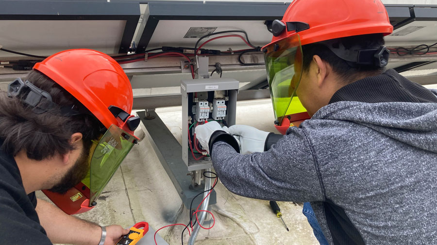 Two students in helmets working in an electrical box
