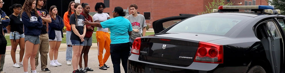 Instructor talking to a group of students in front of a police car