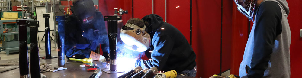 Student welding with two other students in welding helmets watching
