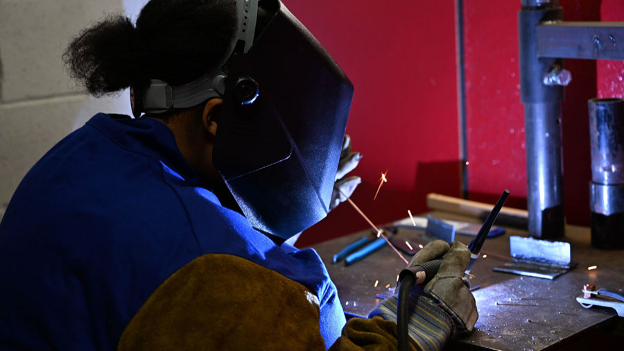 Student in a welding helmet practicing TIG welding