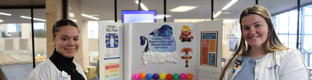 Two people in white lab coats in front of a table with a mental health display on it