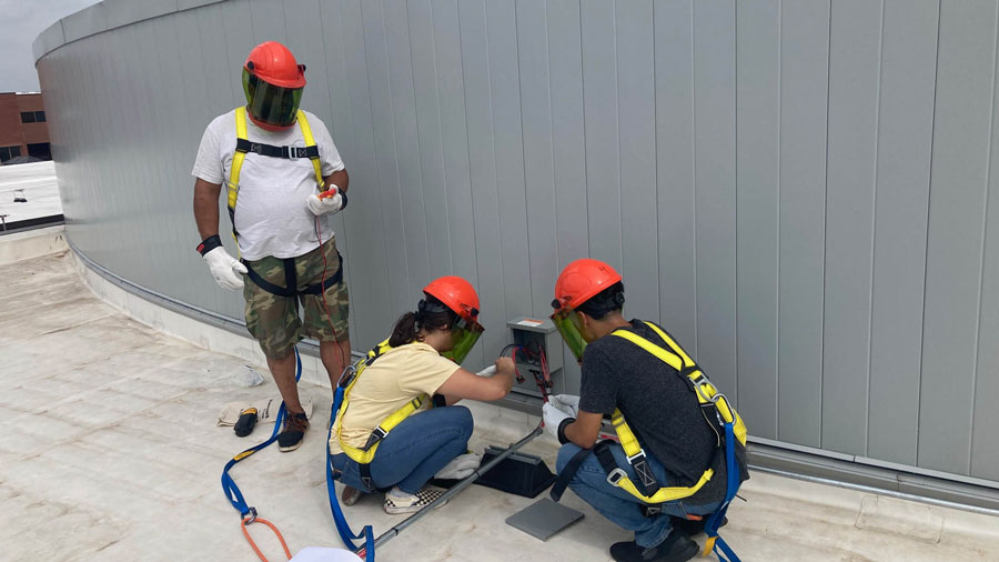 Three students wearing personal protective equipment while working in an electrical box