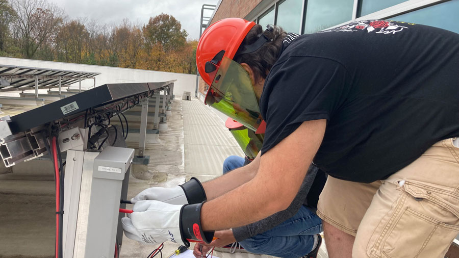 Two students working in an electrical box on the back of a solar panel array
