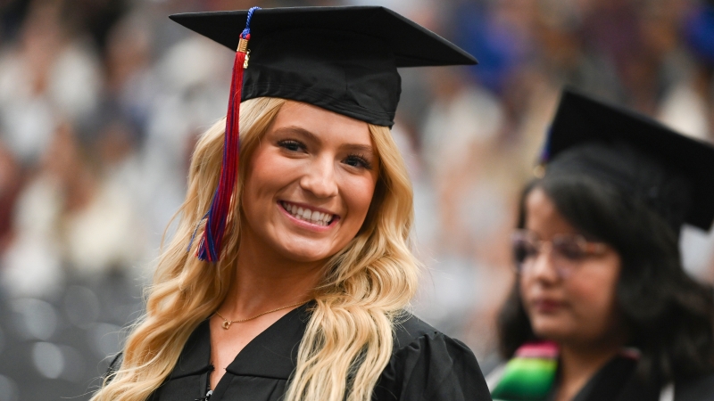 A student in Cap and gown smiling at the camera during the ceremony.