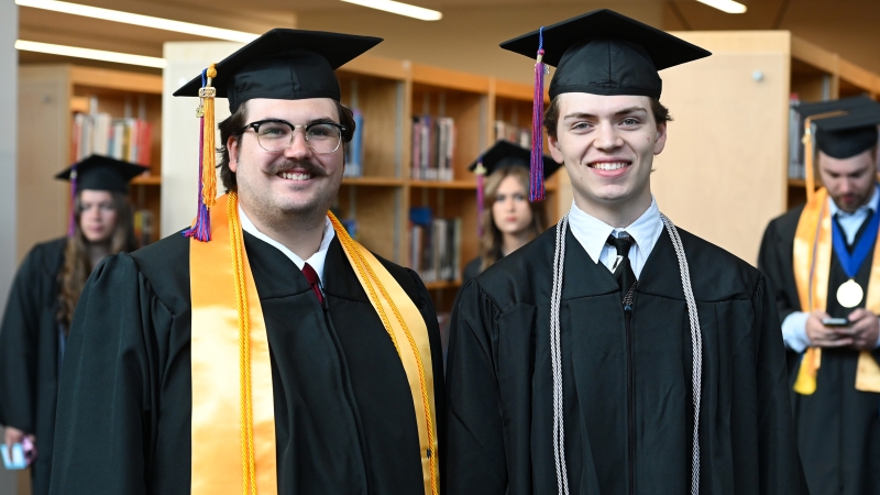 Two students in Cap and gown taking a picture in the library before the graduation ceremony.
