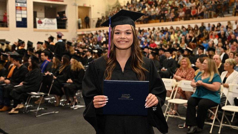 A student in Cap and gown holding on to the KCC Diploma during the graduation ceremony.