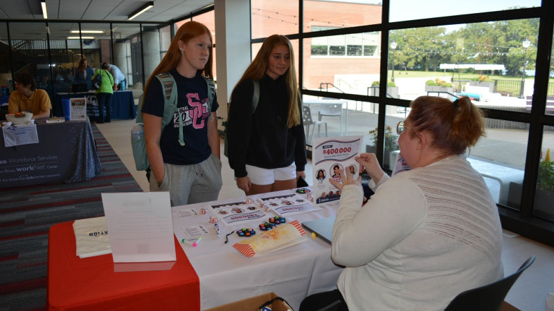 Two students talking to Katie Henry holding up a scholarship flier