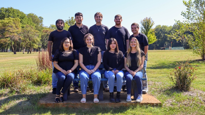Physical Therapist students taking a group picture in all black shirts with denim jeans outside. 